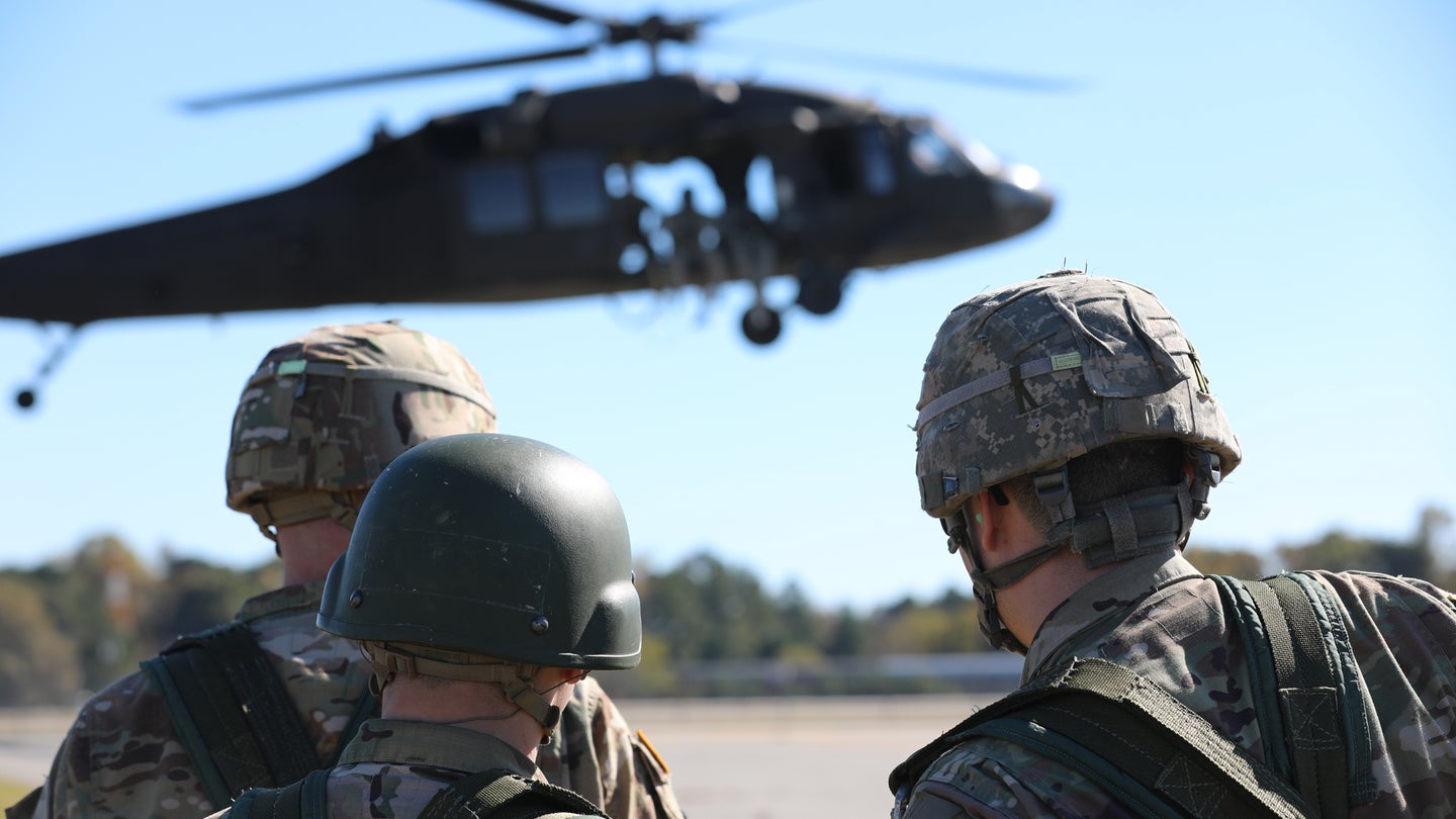 A group of U.S. Army Soldiers, assigned to the 5th Ranger Training Battalion, waits on the Landing Zone to conduct a Speical Patrol Insertion/Extraction (SPIES) attached to a UH-60 Black Hawk Helicopter