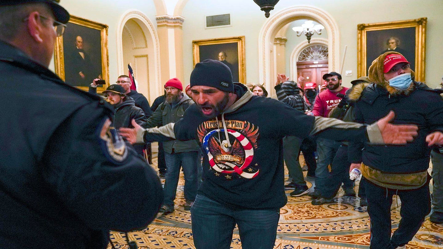 FILE - In this Jan. 6, 2021, file photo, Trump supporters gesture to U.S. Capitol Police in the hallway outside of the Senate chamber at the Capitol in Washington. The U.S. registered its highest deaths yet from the coronavirus on the same day as a mob attack on the nation’s capitol laid bare some of the same, deep political divisions that have hampered the battle against the pandemic. (AP Photo/Manuel Balce Ceneta, File)