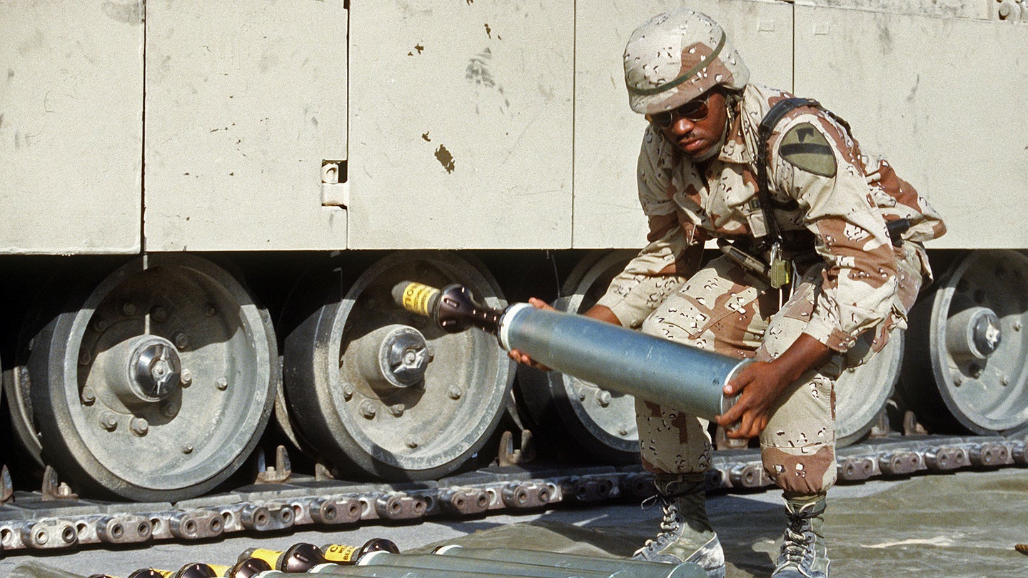 An ammunition specialist carries a 105mm  armor-piercing, discarding sabot round, to be used in an M-1 Abrams main battle tank, during Operation Desert Shield.