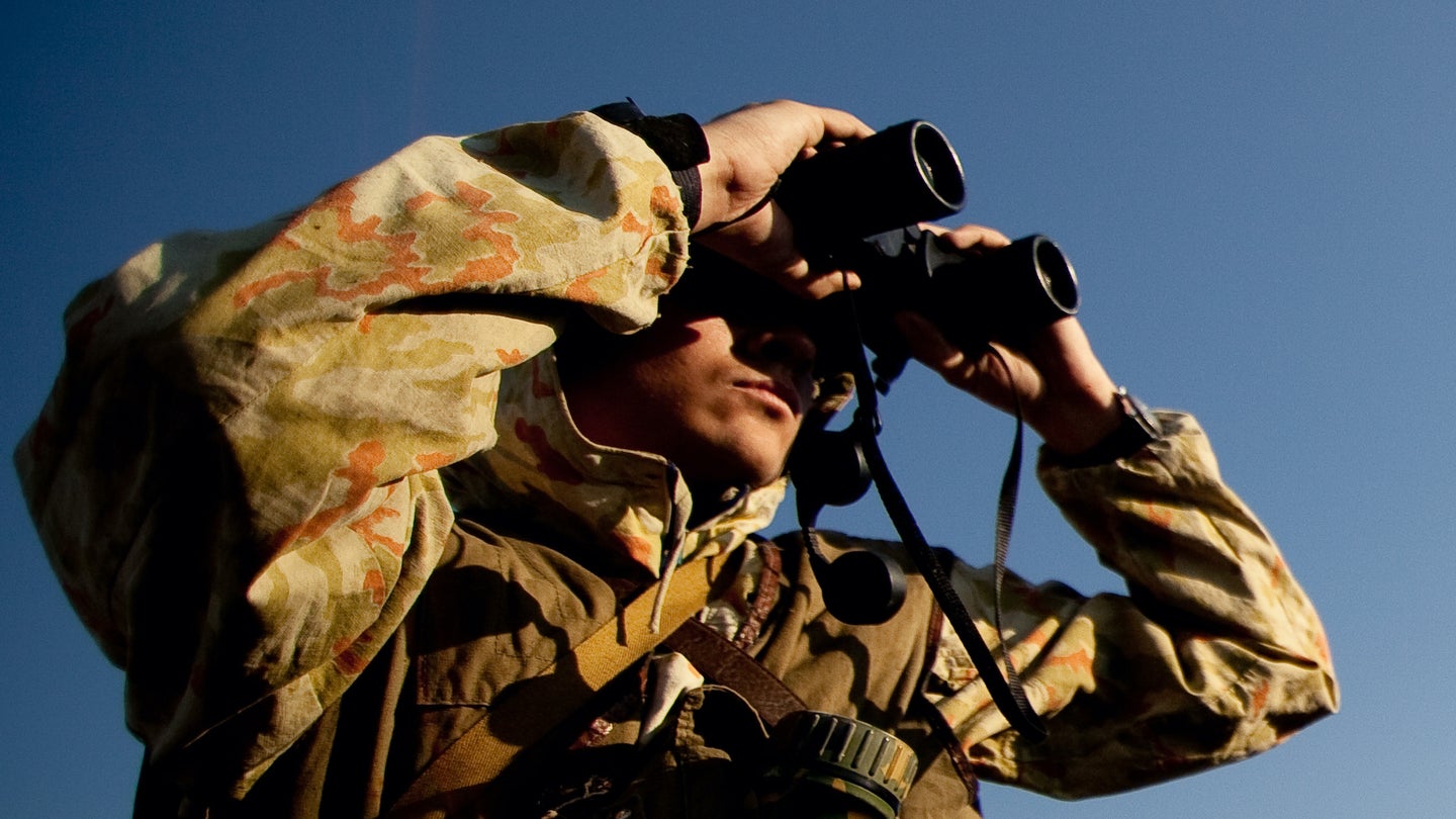A man in camouflage looking through hunting binoculars.