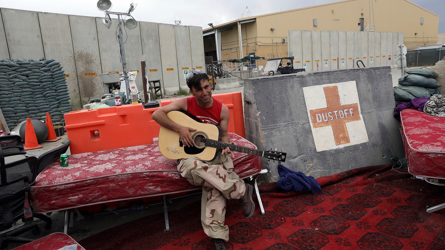 An Afghan soldier plays a guitar that was left behind after the American military departed Bagram air base, in Parwan province north of Kabul, Afghanistan, Monday, July 5, 2021. The U.S. left Afghanistan's Bagram Airfield after nearly 20 years, winding up its "forever war," in the night, without notifying the new Afghan commander until more than two hours after they slipped away. (AP Photo/Rahmat Gul)