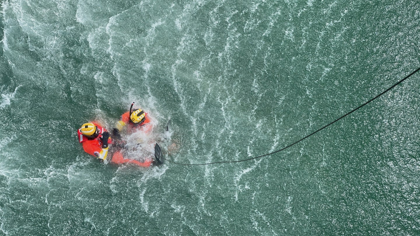 Two members of the Coast Guard, Michael Judin and Chris Moore, in the midst of a practice rescue scenario beneath a helicopter in May, 2021. 