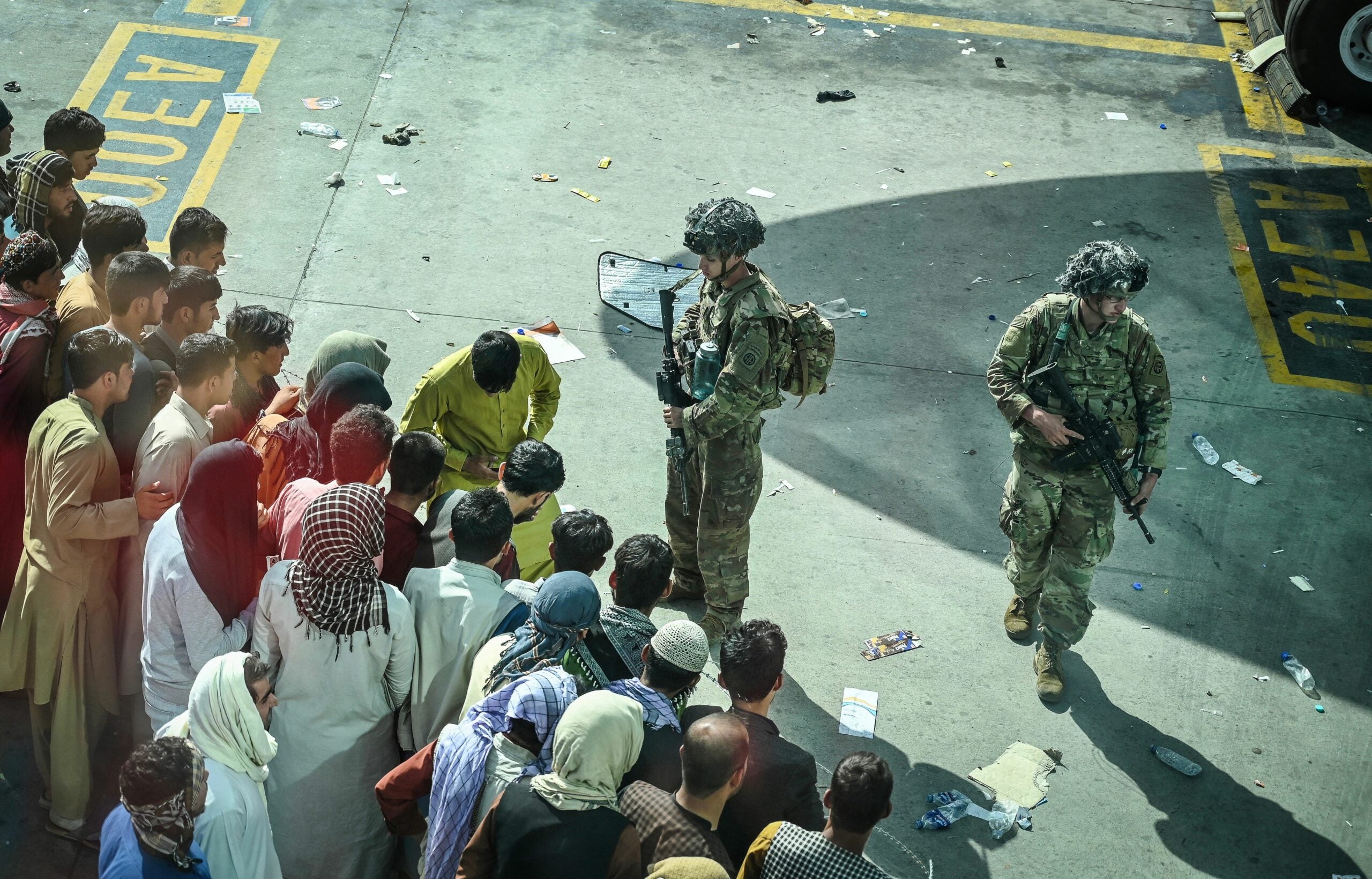 US soldiers stand guard as Afghan people wait at the Kabul airport in Kabul on August 16, 2021, after a stunningly swift end to Afghanistan's 20-year war, as thousands of people mobbed the city's airport trying to flee the group's feared hardline brand of Islamist rule. (Photo by Wakil Kohsar / AFP) (Photo by WAKIL KOHSAR/AFP via Getty Images)