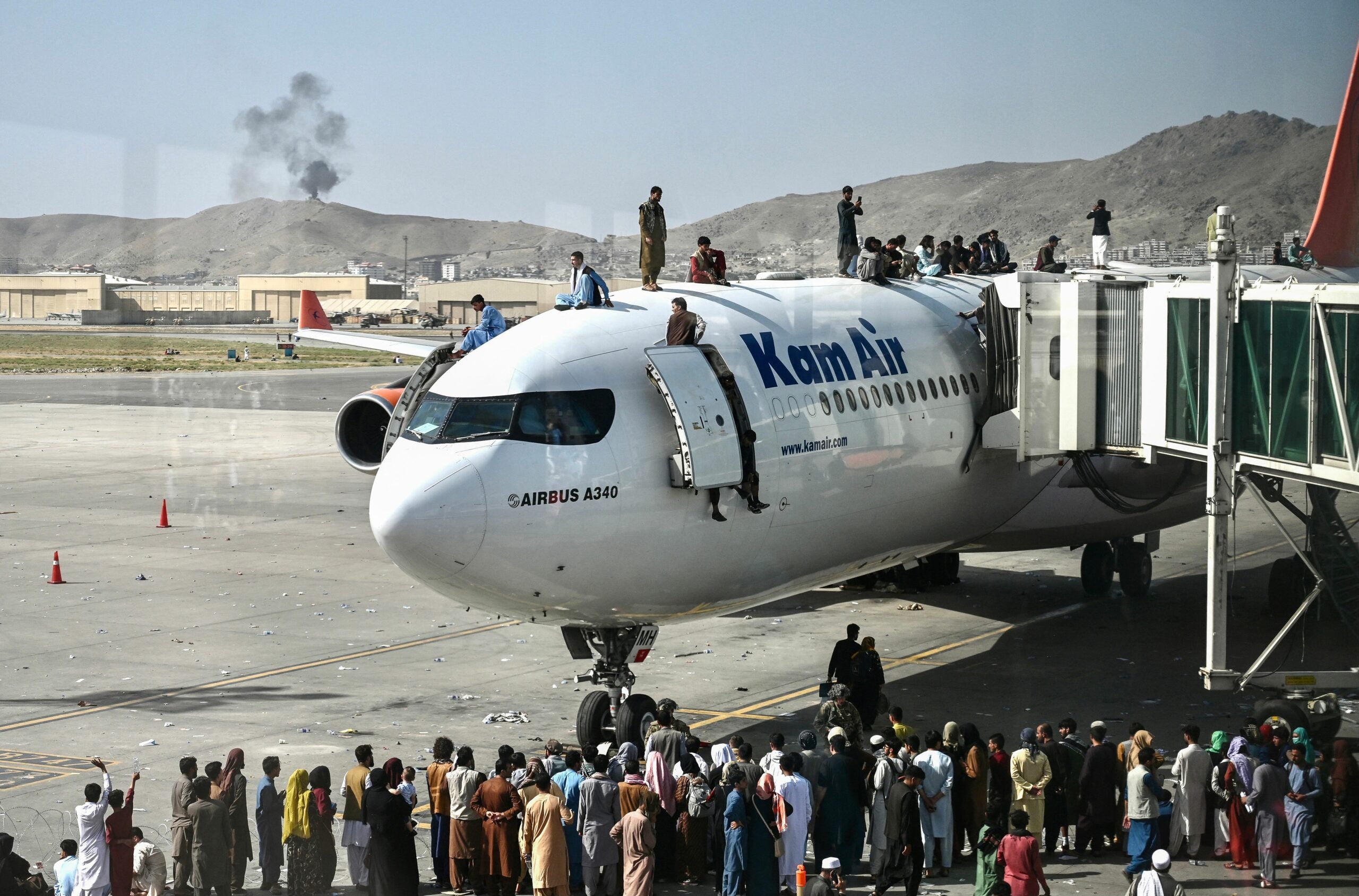 TOPSHOT - Afghan people climb atop a plane as they wait at the Kabul airport in Kabul on August 16, 2021, after a stunningly swift end to Afghanistan's 20-year war, as thousands of people mobbed the city's airport trying to flee the group's feared hardline brand of Islamist rule. (Photo by Wakil Kohsar / AFP) (Photo by WAKIL KOHSAR/AFP via Getty Images)