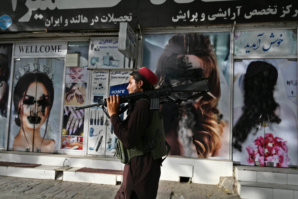 A Taliban fighter walks past a beauty saloon with images of women defaced using a spray paint in Shar-e-Naw in Kabul on August 18, 2021. (Photo by Wakil KOHSAR / AFP) (Photo by WAKIL KOHSAR/AFP via Getty Images)