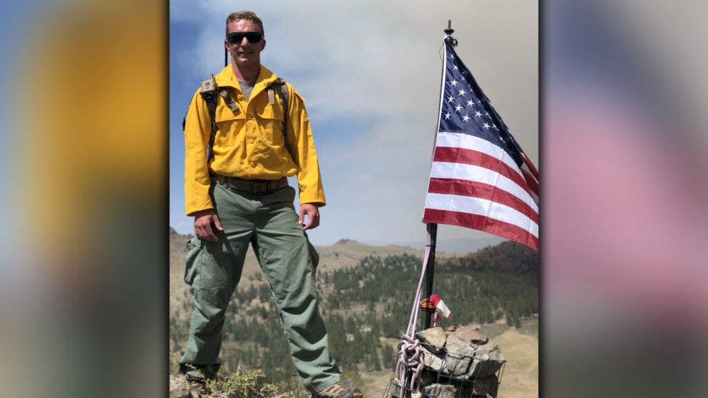 Members of the Pennsylvania Air National Guard are serving as imagery experts, providing live aerial video streaming to fire bosses working on the front lines of the devastating fires. Shown is Staff Sgt. William Gray, Pennsylvania National Guard posing with the American flag on an observation post in western Nevada July 13. (Air National Guard photo by Master Sgt. Brent Hill)