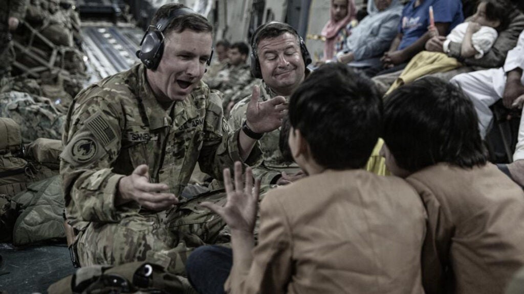 A U.S. soldier with Joint Task Force-Crisis Response (JTF-CR) plays a game on a phone with the children onboard a Boeing C-17 Globemaster III during an evacuation at Hamid Karzai International Airport, Kabul, Afghanistan, Aug. 30, 2021 (U.S. Marine Corps photo by Staff Sgt. Victor Mancillal)