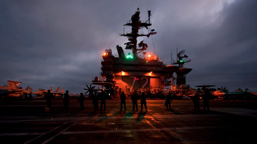 Sailors wait as an MH-60R Sea Hawk helicopter launches from the Nimitz-class aircraft carrier USS Abraham Lincoln. (Photo by Petty Officer 3rd Class Travis K. Mendoza)