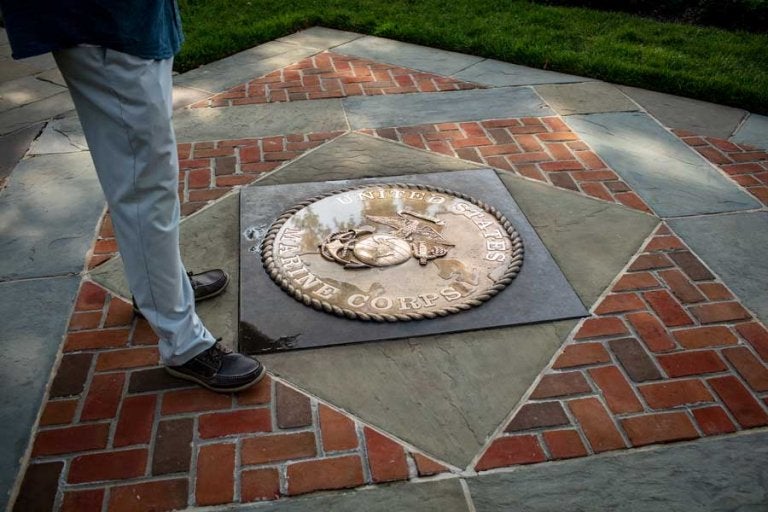 Robert Hogue stands beside the Marine Corps emblem on the patio at Marine Barracks Washington. (Photo by Eliot Dudik, for The War Horse.)