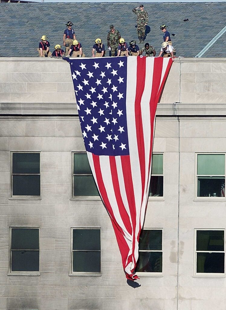 TOPSHOT - Firefighters and soldiers unfurl an American flag from the roof of the damaged side of the Pentagon 12 September 2001 in Washington, DC.  A hijacked airplane crashed into the Pentagon 11 September 2001 causing extensive damage and loss of life.    AFP PHOTO/Luke FRAZZA (Photo by LUKE FRAZZA / AFP) (Photo by LUKE FRAZZA/AFP via Getty Images)