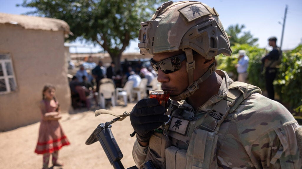 FILE PHOTO: A U.S. Army soldier sips tea passed out by local residents as his commanding officer and allied troops meet with local villagers on May 26, 2021 near the Turkish border in northeastern Syria. (Photo by John Moore/Getty Images)