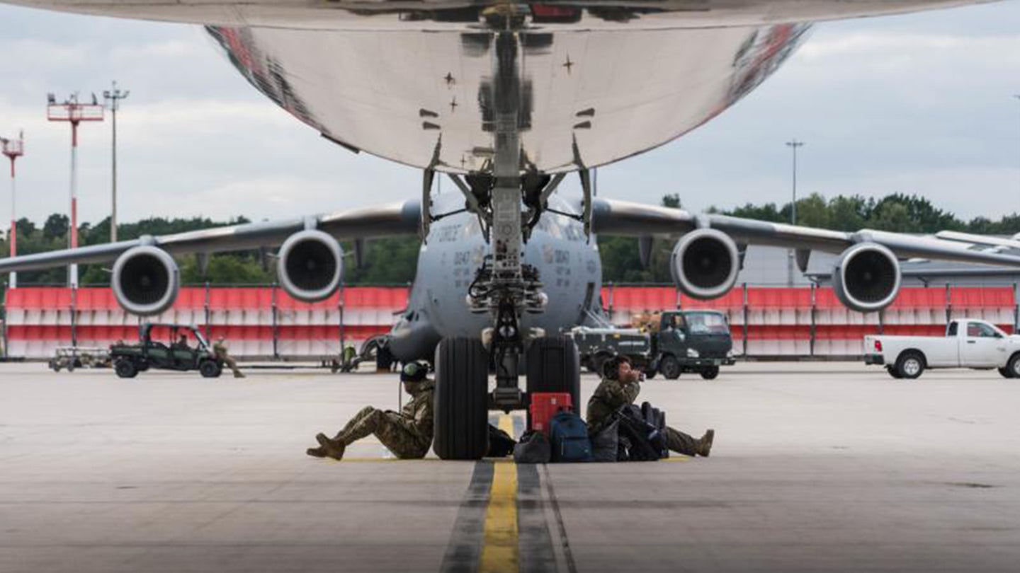 U.S. Air Force Airmen assigned to the 521st Air Mobility Operations Wing rest by the wheel of an aircraft at Ramstein Air Base, Germany, Aug. 27, 2021. Air Mobility Airmen are playing a key role in facilitating the safe departure and relocation of evacuees from Afghanistan during Operation Allies Refuge. (U.S. Air Force photo by Tech. Sgt. Donald Barnec)