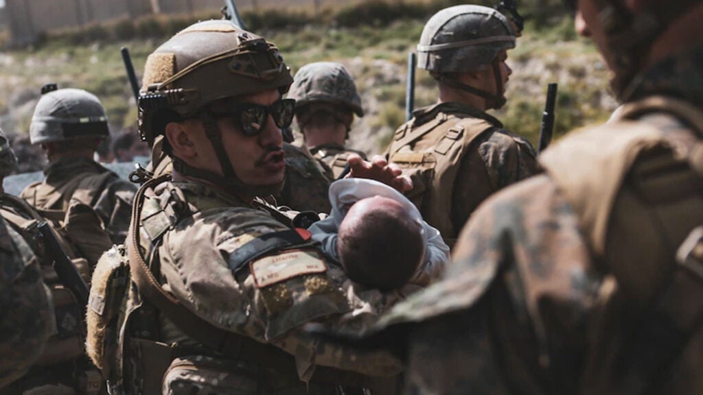 An Airmen comforts an infant during an evacuation at Hamid Karzai International Airport, Kabul, Afghanistan, Aug. 20. U.S. service members and coalition partners are assisting the Department of State with a Non-combatant Evacuation Operation (NEO) in Afghanistan. (Sgt. Isaiah Campbell/U.S. Marine Corps)