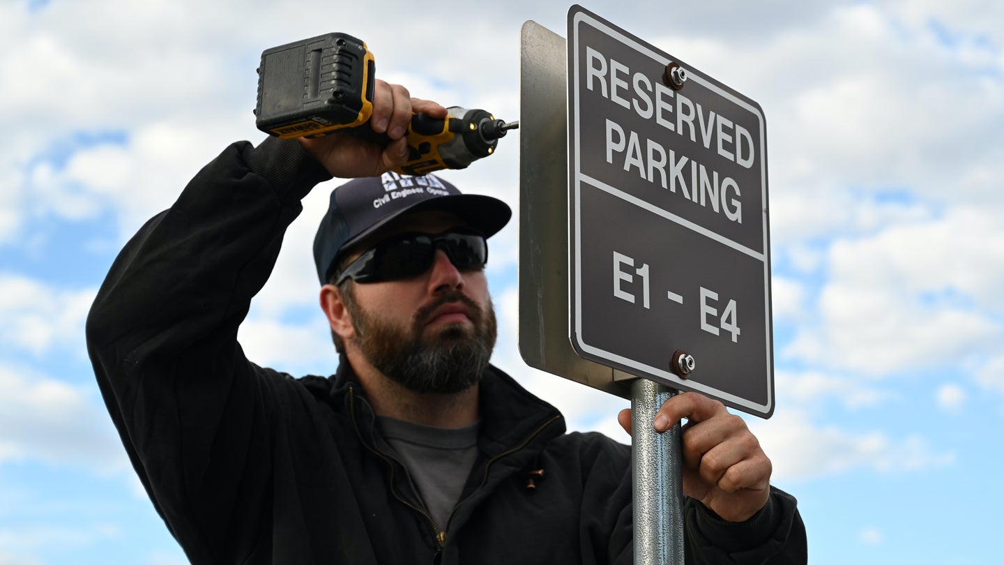 Tyler Adkisson, an equipment operator with Alutiiq, installs new E1-E4 reserved parking signs at the Tinker Exchange parking lot, Tinker Air Force Base, Oklahoma, Oct. 12, 2021. Col. G. Hall Sebren Jr., 72nd Air Base Wing commander, directed that reserved parking for senior leaders be reduced. Some of the previously reserved spaces will be reallocated to junior Airmen, while others are returned to regular shoppers. (U.S. Air Force photo by Paul Shirk)