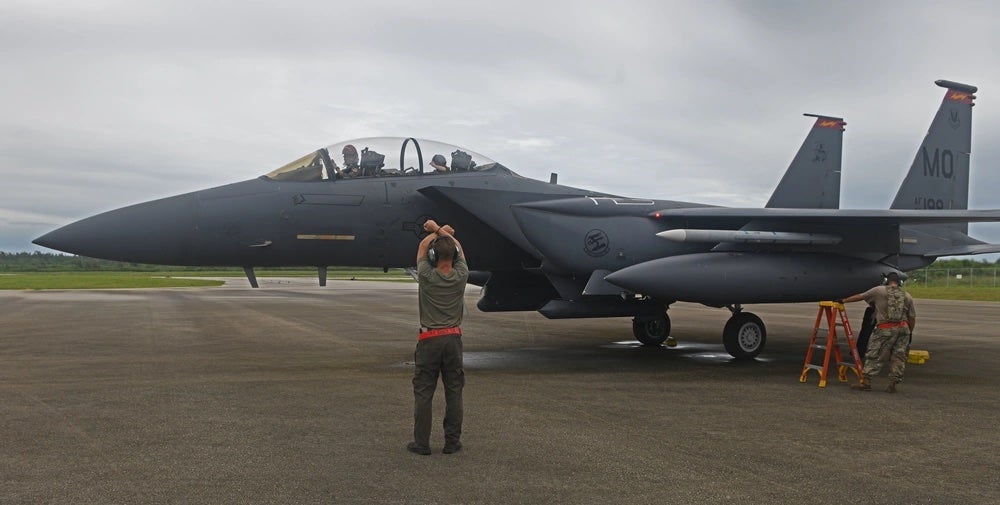 A U.S. Air Force Airman assigned to the 366th Fighter Wing, Mountain Home Air Force Base, Idaho, communicates with hand signals to the aircrew members of an F-15E Strike Eagle while other Airmen perform preflight checks at the Tinian International Airport, Tinian, Aug. 2, 2021, during Pacific Iron 21. (U.S. Air Force photo by Tech. Sgt. Benjamin Sutton)