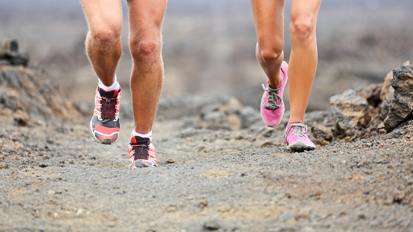 A pair of athletes run along a volcanic path.