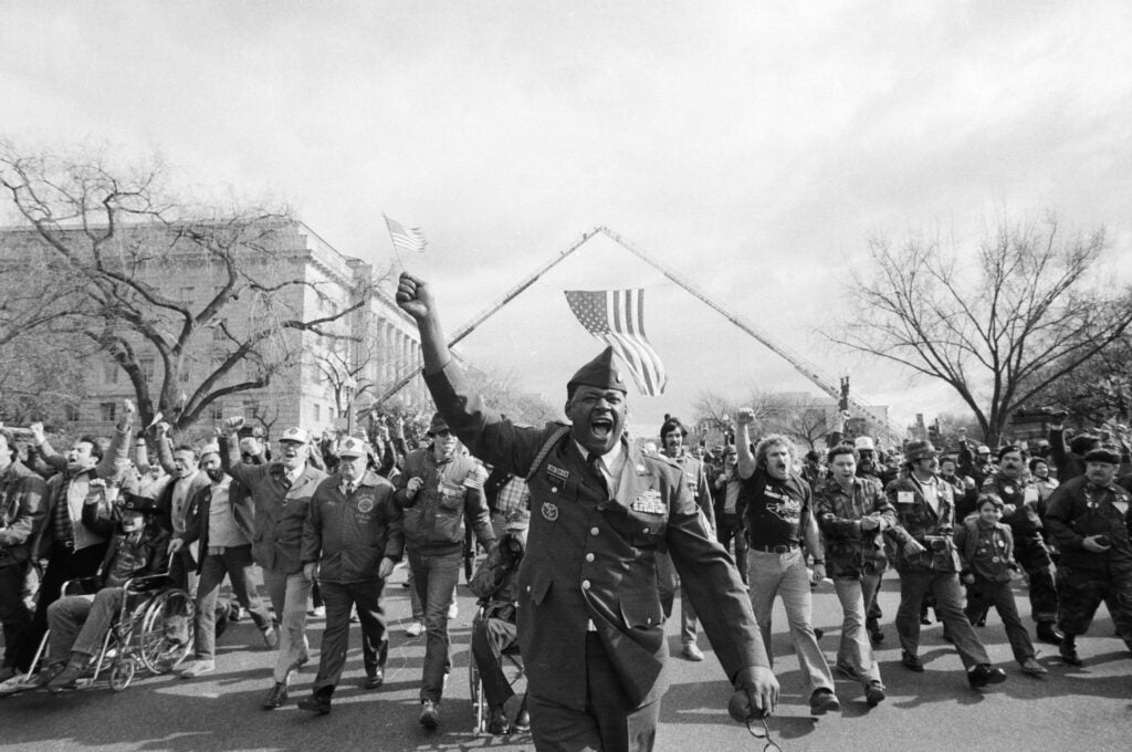 (Original Caption) 11/13/1982- Washington, DC: Vietnam veteran Eugene Brice raises his American flag while marching in the Vietnam Veteran's parade down Constitution Avenue.