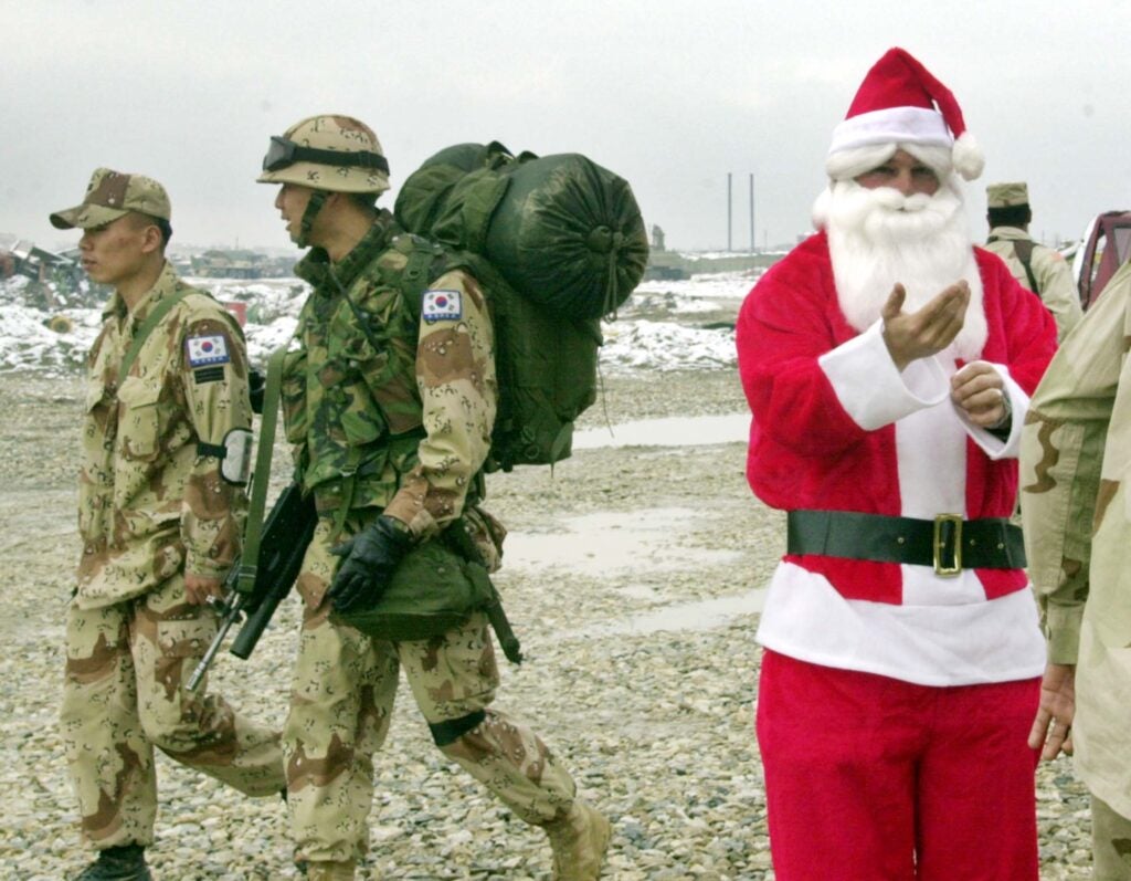 U.S. Army Sgt. Roland Spano Jr. of Baton Rouge, La., dressed as Santa Claus fixes his costume as two South Korean soldiers pass behind him at the new building of the post exchange store Tuesday, Dec. 24, 2002 at Bagram Air Base in Afghanistan. Coalition soldiers stationed at the base do their shopping at the store for their celebration of Christmas. (AP Photo/Pat Roque)