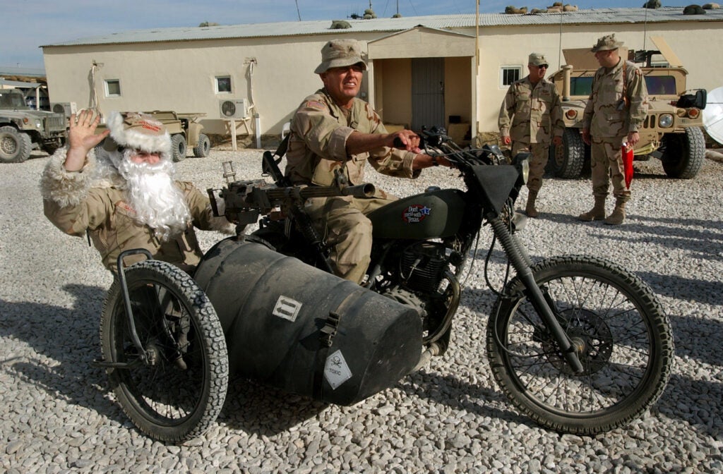 Capt. Clace Perzel, left, rides a military motorcycle side-car dressed as Santa Claus as he bids farewell to troops after distributing gifts to mark Christmas at the U.S base in Ghazni province, west of Kabul, Afghanistan on Christmas eve Saturday Dec. 24, 2005. Others unidentified.(AP Photo/Musadeq Sadeq, Pool)