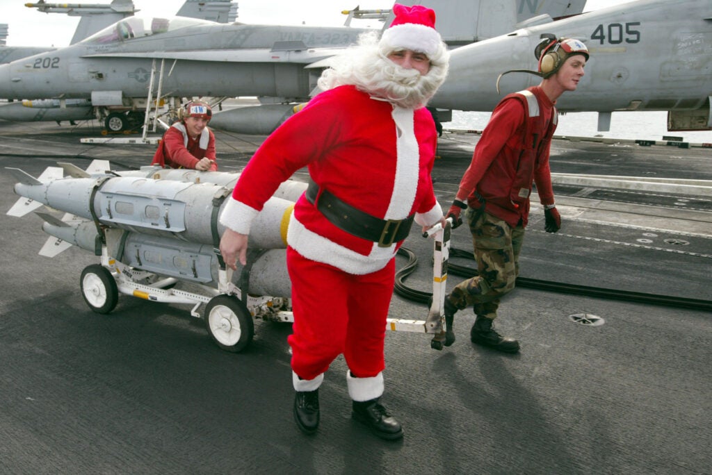 USS CONSTELLATION, THE PERSIAN GULF - DECEMBER 24:  U.S. Navy sailor Rick Pellicciotti from Follansbee, West Virginia, dressed as Santa Claus helps wheel a load of bombs to fighter planes on the deck of the USS Constellation December 24 , 2002 in the Persian Gulf. The crew of the aircraft carrier celebrated Christmas one day early because they have a full day of work on Christmas day. The war planes from the aircraft carrier have the mission to patrol the no-fly zone in southern Iraq. The no-fly zones in southern and northern Iraq were established after the 1991 Persian Gulf war to prevent Iraq from carrying out airstrikes against Shiites in southern Iraq and Kurdish forces in the north of the country. The zones have been patrolled by the United States Air Force and Navy and by the British.  (Photo by Joe Raedle/Getty Images)
