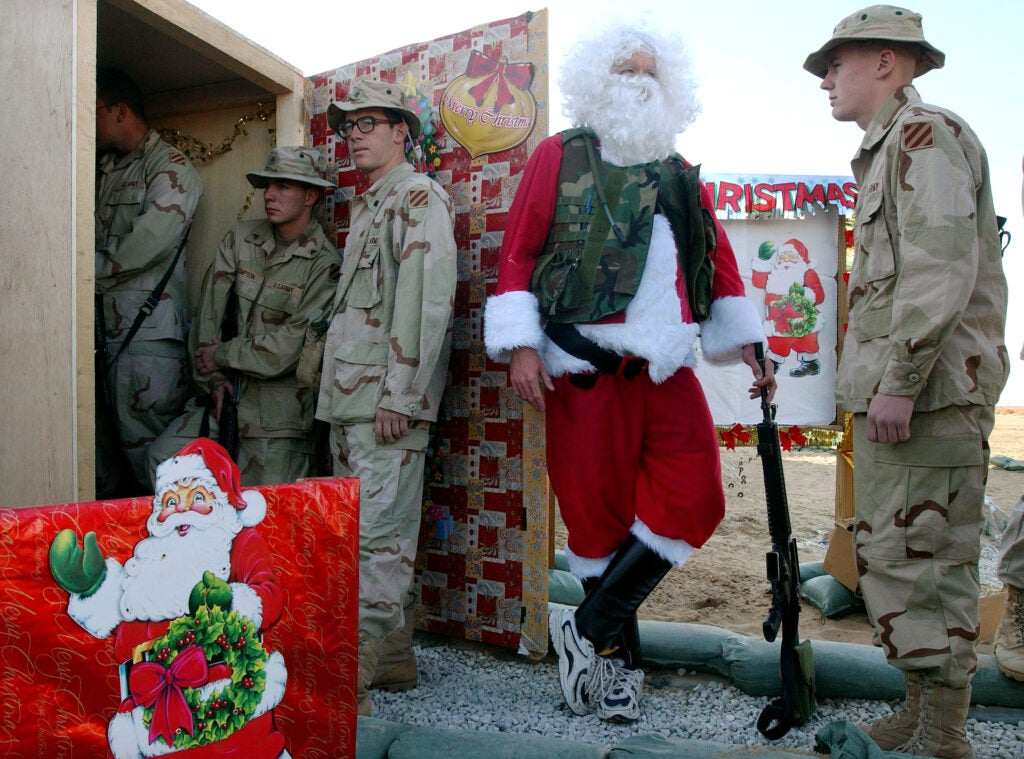 CAMP VIRGINIA, KUWAIT - DECEMBER 25:  U.S. Army Captain William T. Johnson, from Richmond, Virginia, wears a Santa Claus outfit with a camouflage flak jacket and carries an M-16 rifle as he welcomes soldiers to Christmas dinner December 25, 2002 at Camp Virginia in the Kuwaiti desert. More than 10,000 soldiers are spending the holidays away from their families while on exercises in Kuwait near the Iraqi border.  (Photo by Scott Nelson/Getty Images)