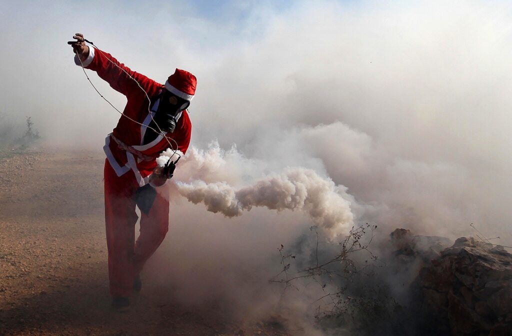 RAMALLAH, WEST BANK - DECEMBER 26: A Palestinian, wears a Santa Claus costume, throws a tear gas capsule back to the Israeli security forces during a protest against the separation barrier (wall) and Jewish settlement construction at Bilin Village, in Ramallah, West Bank on December 26, 2014. (Photo by Issam Rimawi/Anadolu Agency/Getty Images)