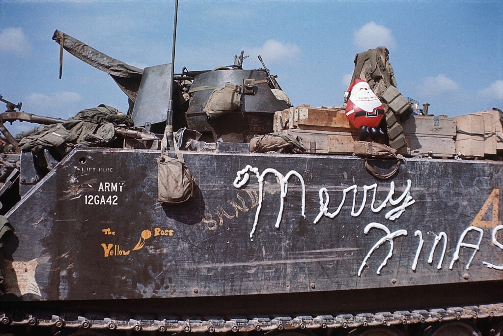 (Original Caption) 12/25/1969-Cu Chi, South Vietnam- During a Christmas cease fire 12/25 at Fire Base Evans, 40 miles west of Saigon, troops relaxed, cleaned equipment, attended religious services and set up a small Santa Claus and a little Christmas tree atop an armored vehicle, shown here with a shaving cream "Merry Christmas" scored on its side.