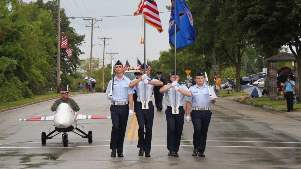 Ron Koplin, the commander of the Civil Air Patrol Timmerman Composite Squadron, drives a mini F-16 alongside a marching band in a Wisconsin parade. (Photo courtesy Ron Koplin / CAP Timmerman)