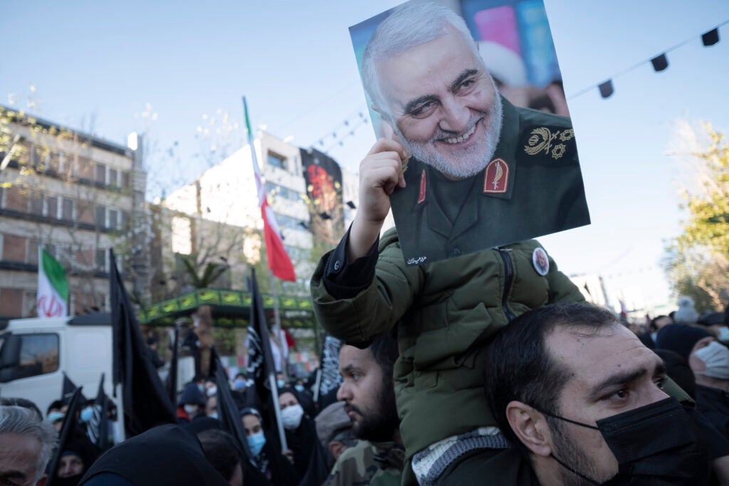 An Iranian young boy holds a portrait of former commander of the Islamic Revolutionary Guard Corps (IRGC) Quds Force General Qasem Soleimani who has killed in a U.S. drone attack in Baghdad in 2020, while attending a funeral for the Iran-Iraq war (1980-88) unknown martyrs in downtown Tehran on January 6, 2022. Thousands of Iranians attend a funeral for 150 Iran-Iraq war (1980-88) unknown Martyrs that have found by the Iranian Martyrs investigation group in the war main field  34-years after a ceasefire between Iran and Iraq in 1988. (Photo by Morteza Nikoubazl/NurPhoto via Getty Images)
