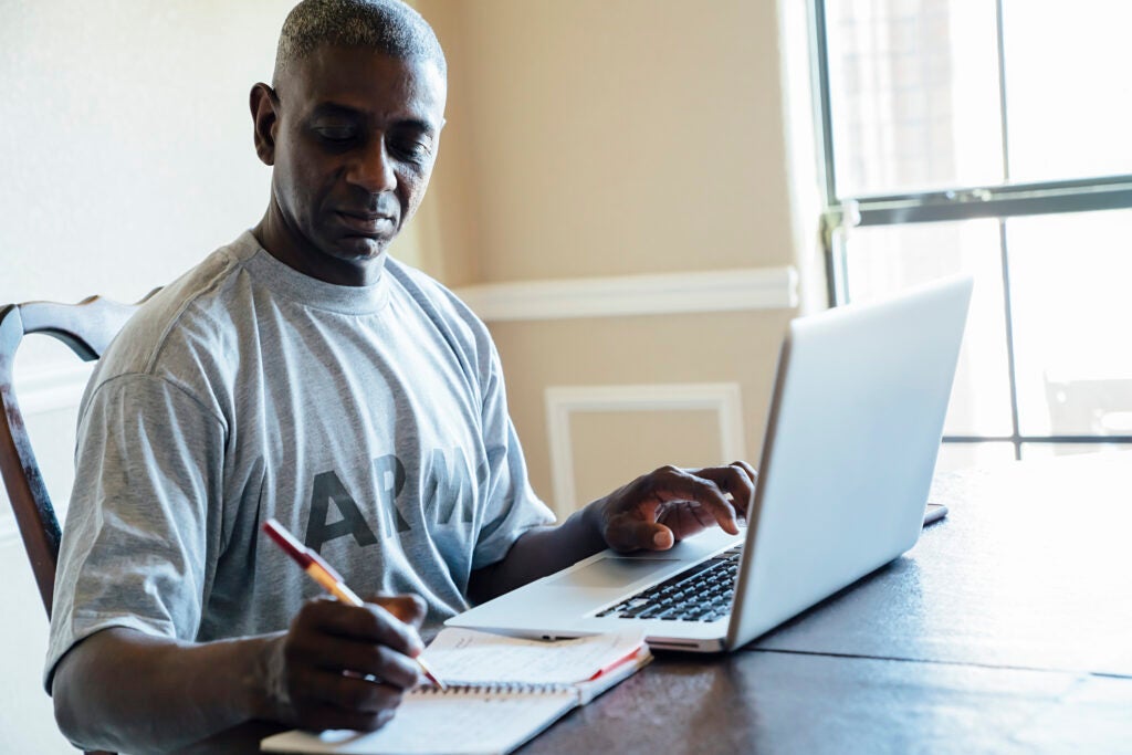 Black man using laptop and notebook at table