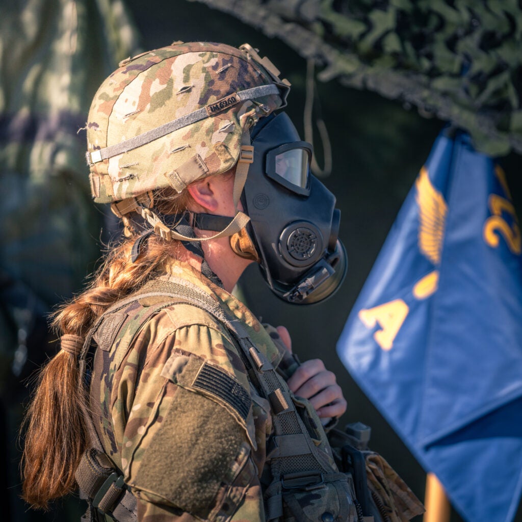 A female soldiers wear a ponytail with helmet and gas mask.