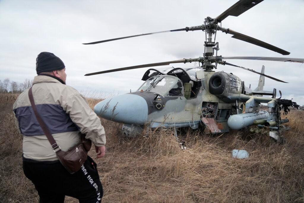 A man stands in front of a Russian Ka-52 helicopter gunship is seen in the field after a forced landing outside Kyiv, Ukraine, Thursday, Feb. 24, 2022. Russia on Thursday unleashed a barrage of air and missile strikes on Ukrainian facilities across the country. (AP Photo/Efrem Lukatsky)