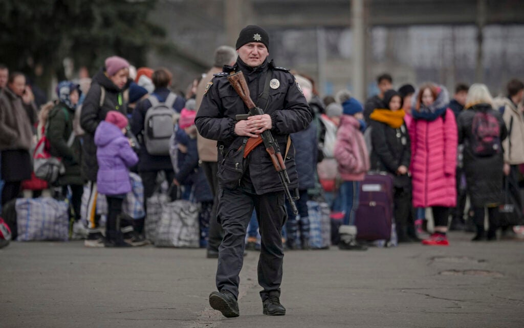 A Ukrainian police officer carrying an assault rifle walks on a platform backdropped by people waiting for a Kiev bound train in Kostiantynivka, Donetsk region, eastern Ukraine, Thursday, Feb. 24, 2022. Russia launched a wide-ranging attack on Ukraine on Thursday, hitting cities and bases with airstrikes or shelling, as civilians piled into trains and cars to flee.  (AP Photo/Vadim Ghirda)