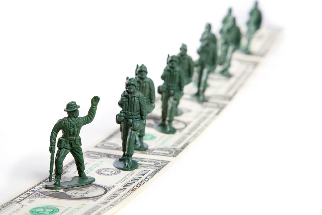 A line of toy plastic soldiers marching on a road made of dollar bills.