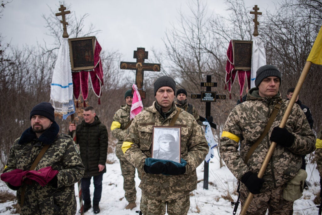 BILA KRYNYTSIA, UKRAINE - MARCH 6: Ukrainian soldiers are holding the portrait and the medals of Denys Hrynchuk during the service at the cemetery in Bila Krynytsia, on March 6, 2022 in Chernivtsi region, Ukraine. Denys Hrynchuk served in the Ukrainian army. He was killed on February 28, 2022, near Volnovakha, Donetsk region. He is survived by his mother, five brothers and a sister, his wife and his one-year-old son. Ukrainians from the eastern and central parts of the country have increasingly fled to western cities as Russian forces advance toward Kyiv from three sides. Russia's large-scale invasion of Ukraine has prompted widespread condemnation from European countries, coupled with sanctions on Russia and promises of military support for Ukraine. (Photo  by Alexey Furman/Getty Images)