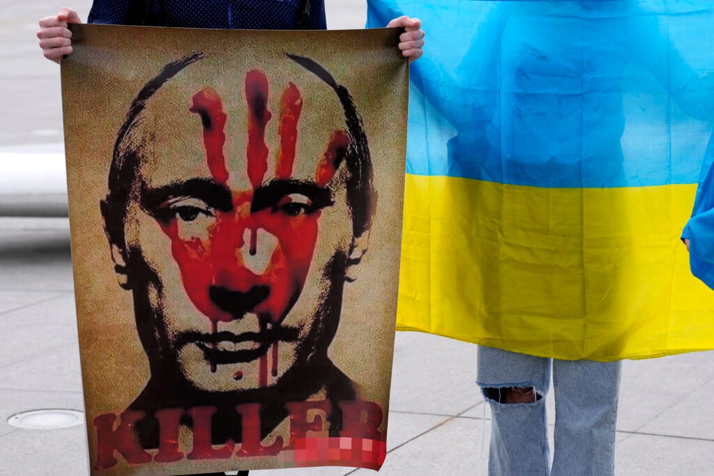 A protester holds a placard showing the Russian president Vladimir Putin as an other protester holds a Ukrainian flag during a protest against Russia's invasion of Ukraine at Elephtheria, Liberty, square in central Nicosia, Cyprus, Saturday, March 5, 2022. What looked like a breakthrough cease-fire to evacuate residents from two cities in Ukraine quickly fell apart Saturday as Ukrainian officials said shelling had halted the work to remove civilians hours after Russia announced the deal. (AP Photo/Petros Karadjias)