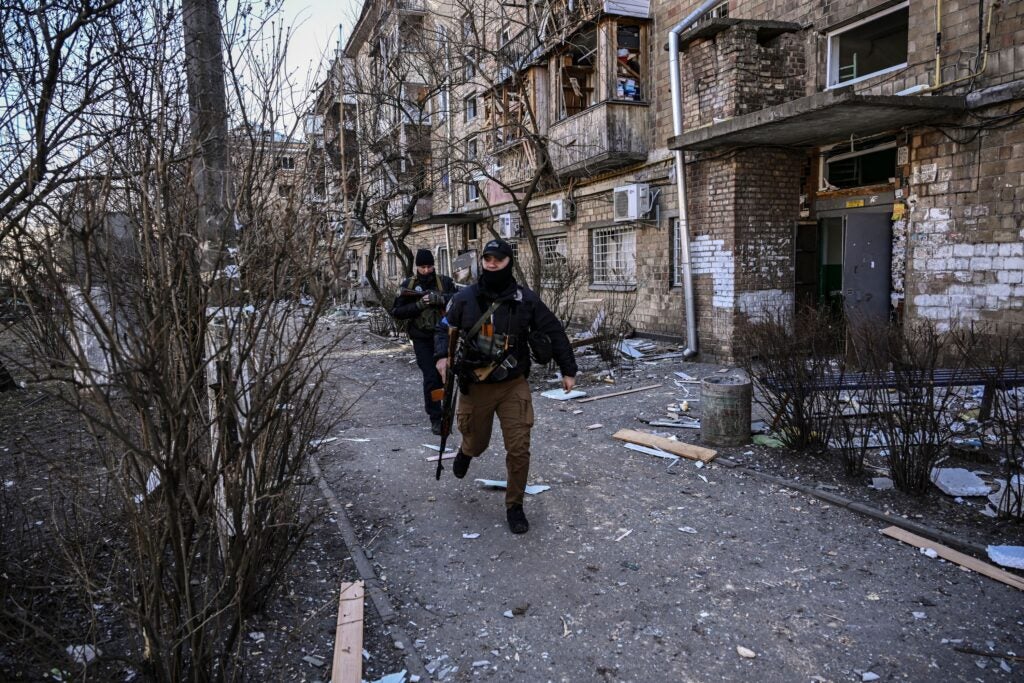 Ukranian servicemen run outside a destroyed apartment building in a residential area after shelling in Kyiv on March 18, 2022, as Russian troops try to encircle the Ukrainian capital as part of their slow-moving offensive. - Authorities in Kyiv said one person was killed early today when a downed Russian rocket struck a residential building in the capital's northern suburbs. They said a school and playground were also hit. (Photo by Aris Messinis / AFP) (Photo by ARIS MESSINIS/AFP via Getty Images)