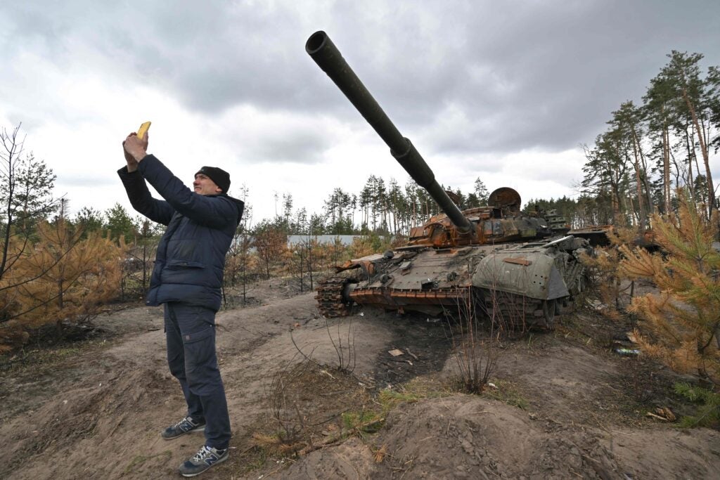 TOPSHOT - A man takes a selfie as he stands in front of a destroyed Russian tank in the vilage of Andriivka, in the Kyiv region on April 17, 2022. - Russia invaded the Ukraine on February 24, 2022. (Photo by Sergei SUPINSKY / AFP) (Photo by SERGEI SUPINSKY/AFP via Getty Images)