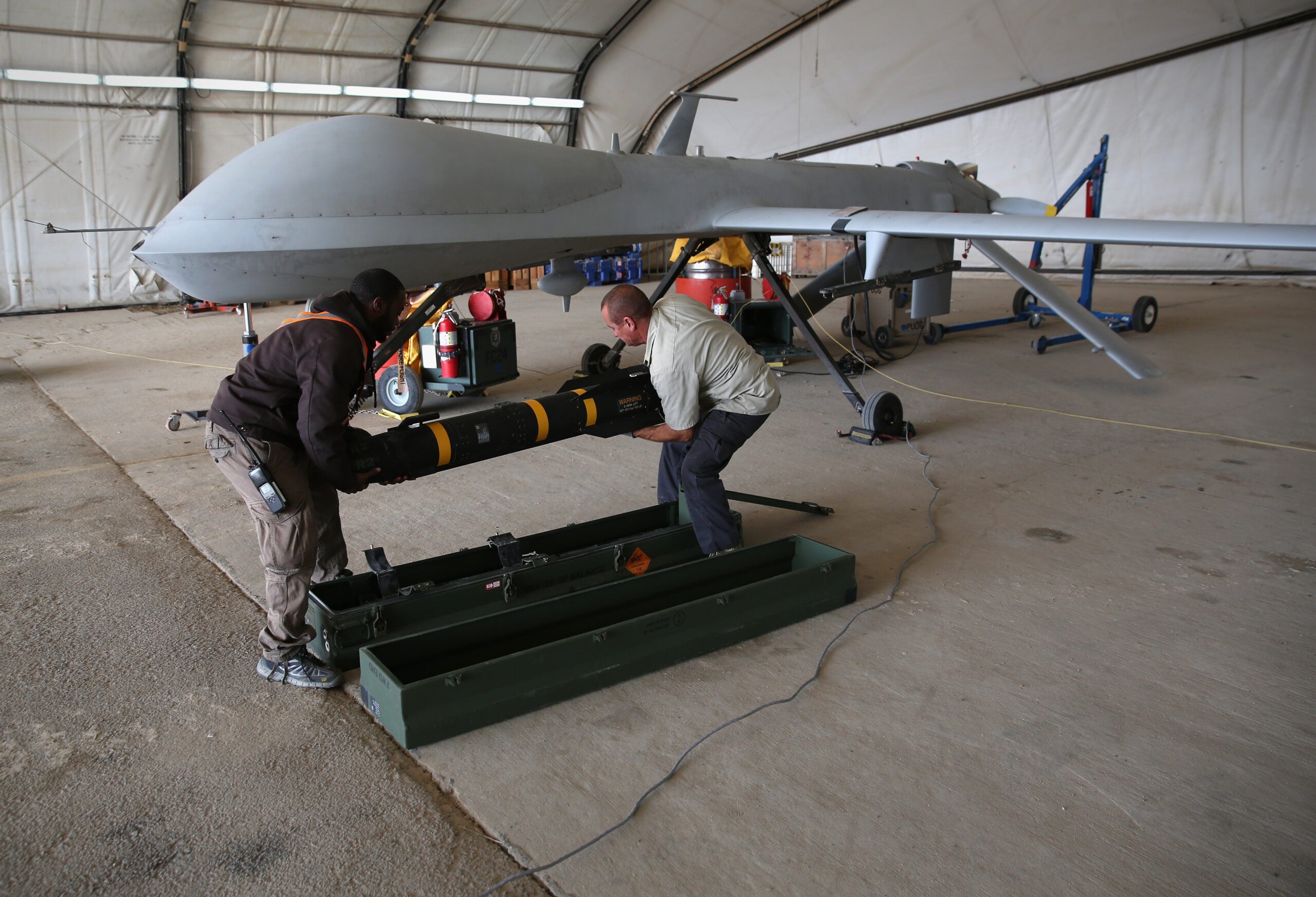 UNSPECIFIED, UNSPECIFIED - JANUARY 07:  Contract workers load a Hellfire missile onto a U.S. Air Force MQ-1B Predator unmanned aerial vehicle (UAV), at a secret air base in the Persian Gulf region on January 7, 2016. The U.S. military and coalition forces use the base, located in an undisclosed location, to launch drone airstrikes against ISIL in Iraq and Syria, as well as to distribute cargo and transport troops supporting Operation Inherent Resolve. The Predators at the base are operated and maintained by the 46th Expeditionary Reconnaissance Squadron, currently attached to the 386th Air Expeditionary Wing.  (Photo by John Moore/Getty Images)