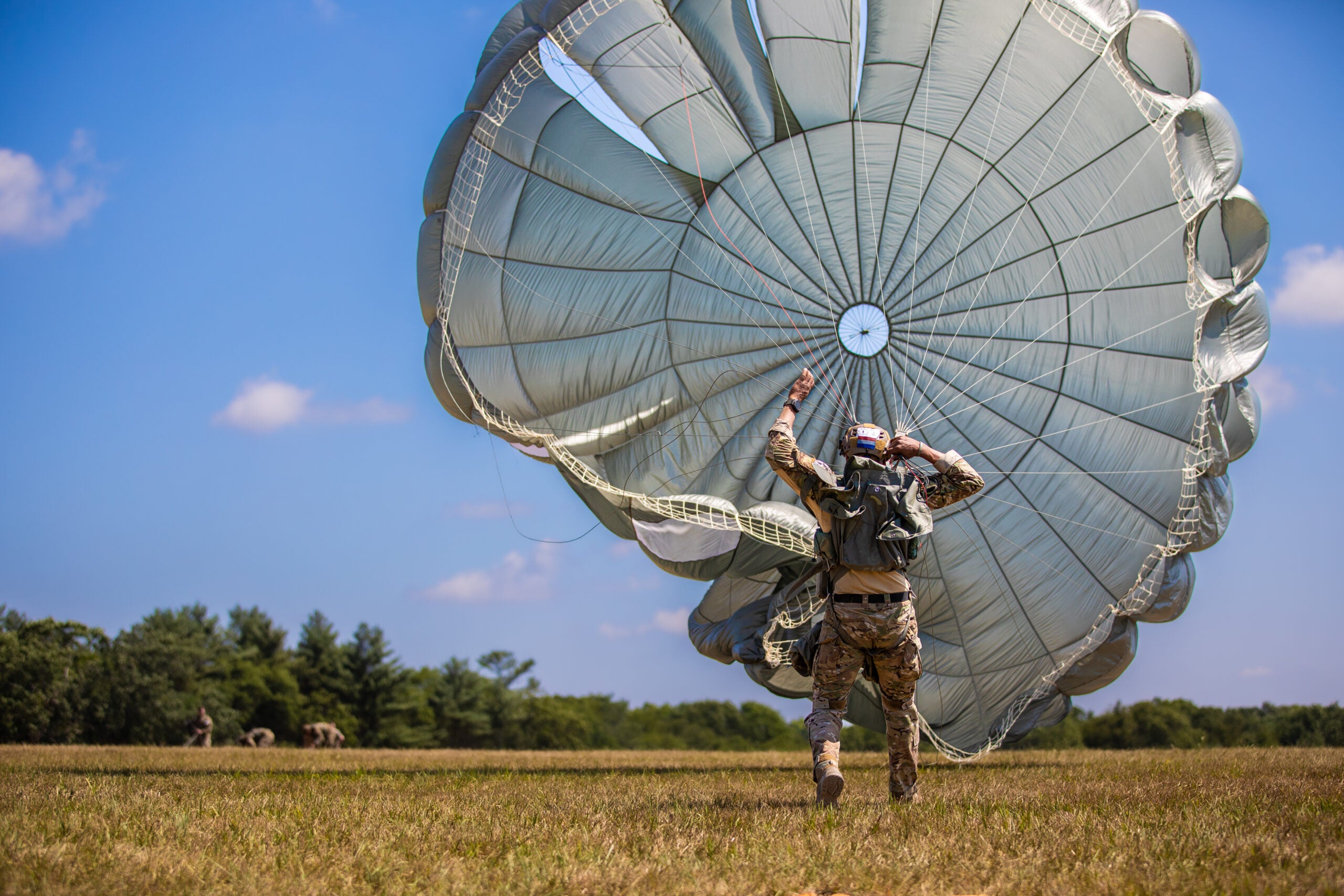 A Dutch Paratrooper drags his MC-6 parachute towards the objective on Glen Rock Drop Zone during Leapfest 2022 at Exeter, Rhode Island, August 6, 2022. Leapfest is the largest, longest standing, international static line parachute training event and competition hosted by the 56th Troop Command, Rhode Island Army National Guard to promote high level technical training and esprit de corps within the International Airborne community. (U.S. Army Reserve photo by Sgt. Eric Kestner)