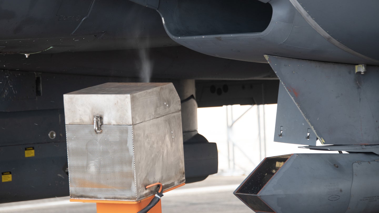 Analysts from the Air Force Research Laboratory's 711th Human Performance Wing use the orange spray carts displayed to insert oil of wintergreen into the idling F-15E Strike Eagle prior to taxi at Eglin Air Force Base, Fla., Aug. 16, 2022. This test is part of a larger Department of Defense effort to evaluate cockpit environmental conditions after a chemical weapon attack (Ilka Cole/U.S. Air Force)