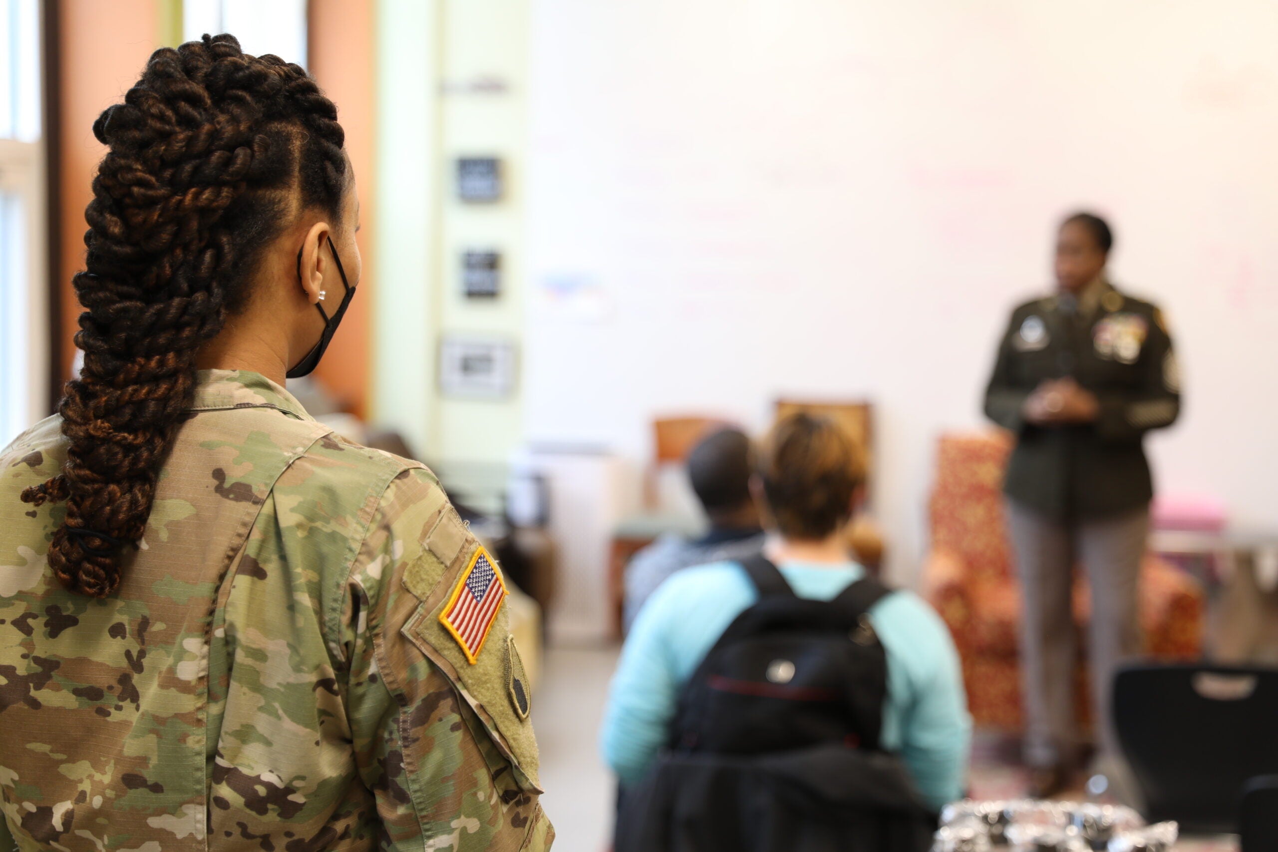 Staff Sgt. Devera Arnwine, recruiting and retention noncommissioned officer, Maryland Army National Guard, looks on as Command Sgt. Maj. Perlisa Wilson, senior enlisted leader of the Maryland National Guard, speaks to students about benefits and career opportunities in the MDNG at City Neighbors High School in Baltimore on April 7, 2022. Arnwine's area of operation for recruiting is in Baltimore. (U.S. Army National Guard photo by Staff Sgt. Chazz Kibler)