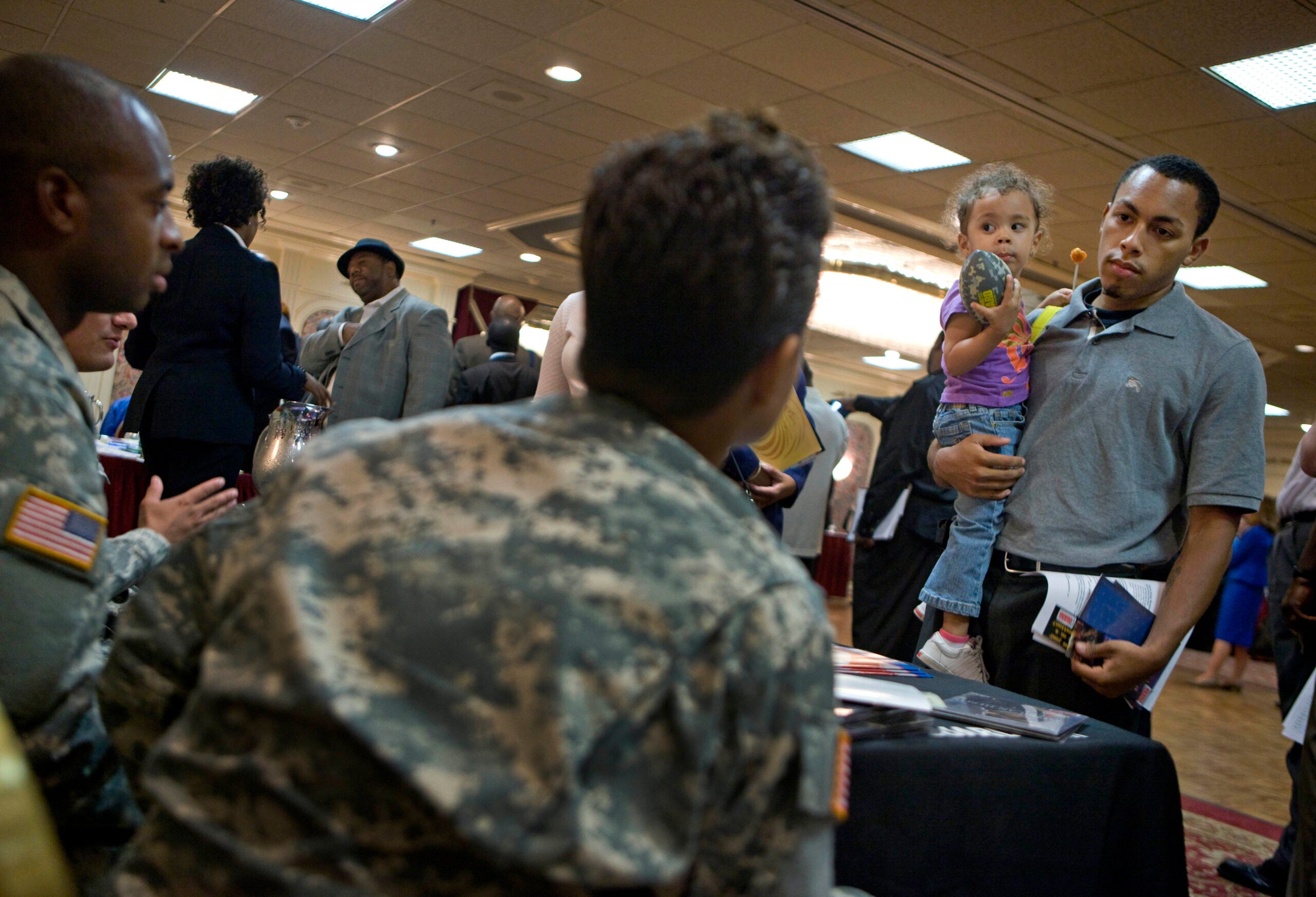 In this Aug. 24, 2010 photograph, Aaron Harvey, of Elizabeth, N.J., holds his daughter Grace, 2, while talking to U.S. Army National Guard recruiters about enlisting at a career fair in Newark, N.J. (AP Photo/David Goldman)
