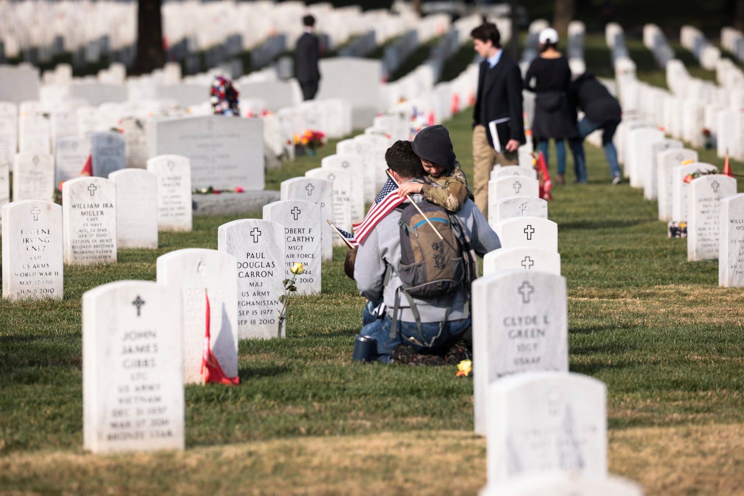 ARLINGTON, VIRGINIA - NOVEMBER 11: Army veteran Stephen Hedger is hugged by his son Lincoln as he visits the gravesite of U.S. Army Major Paul Douglas Carron at Arlington National Cemetery on Veterans Day, November 11, 2021 in Arlington, Virginia. During Veteran's Day, military members, veterans and their loved ones visited the cemetery to pay their respects to those they have lost. (Photo by Anna Moneymaker/Getty Images)