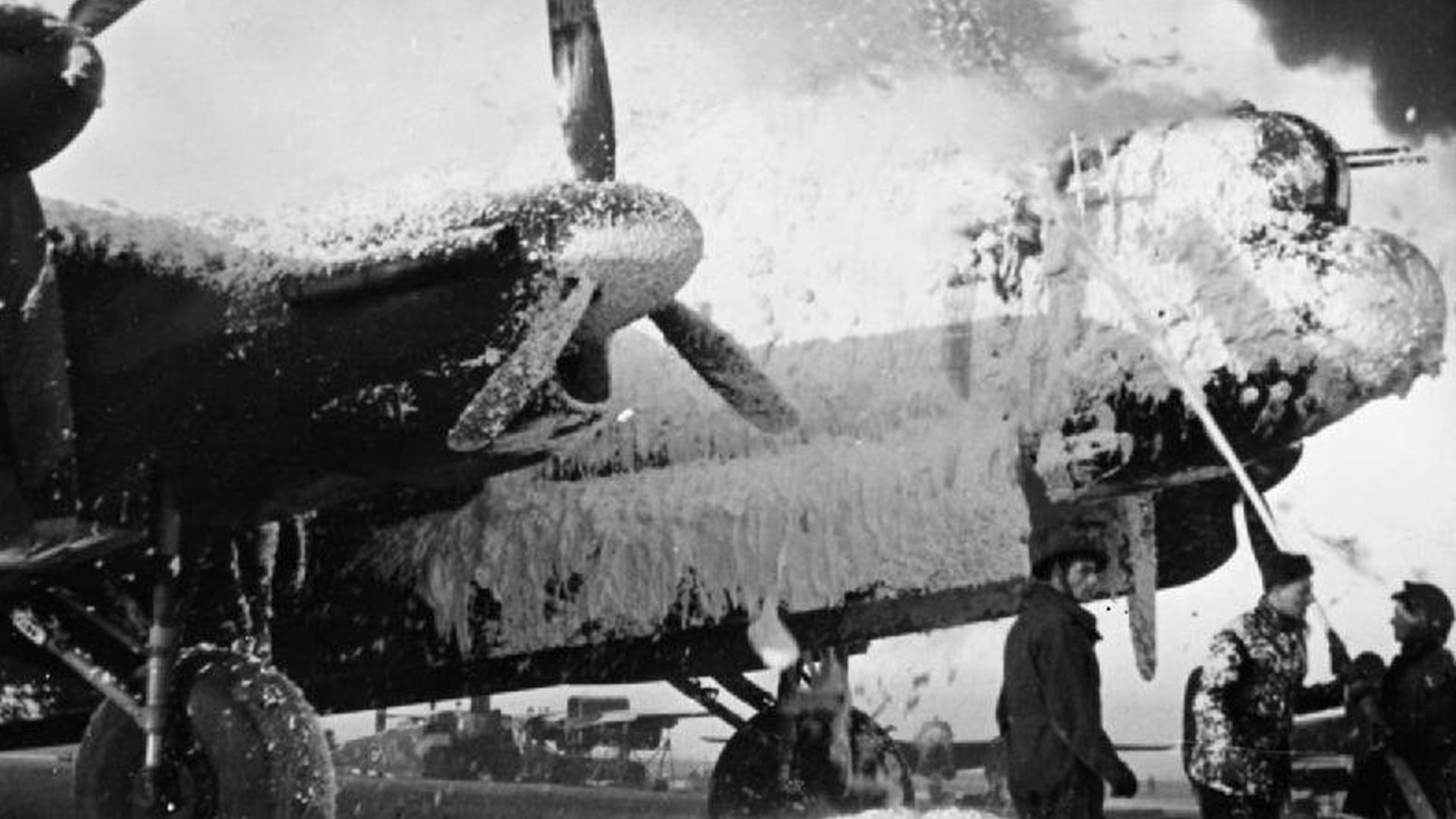Fire crews cover an Avro Lancaster of Bomber Command with foam in an effort to save it from burning, at B58/Melsbroek, Belgium, following the attack on the airfield by Luftwaffe fighter-bombers in Operation Bodenplatte during World War II. (Royal Air Force)