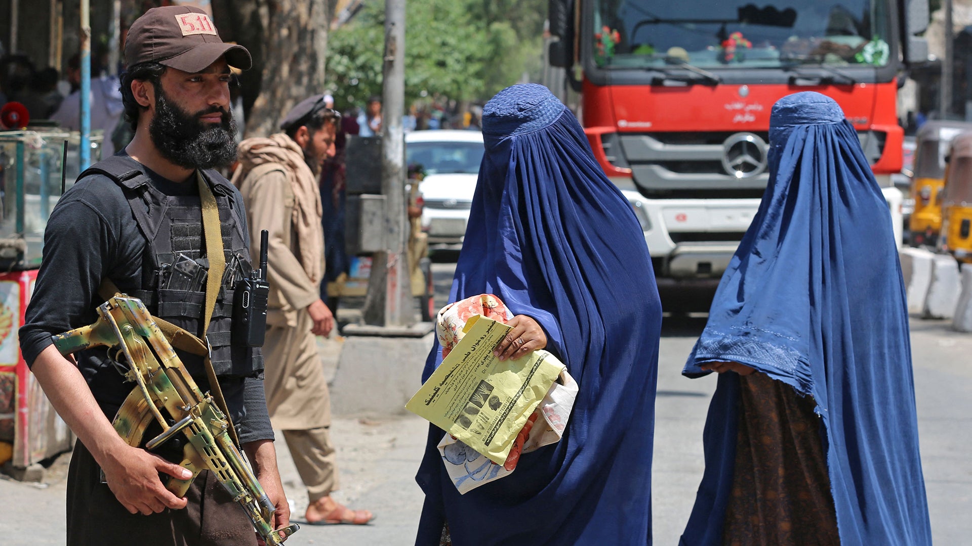 TOPSHOT - Afghan burqa-clad women walk past a Taliban security personnel along a street in Jalalabad on April 30, 2023. (Photo by Shafiullah KAKAR / AFP) (Photo by SHAFIULLAH KAKAR/AFP via Getty Images)