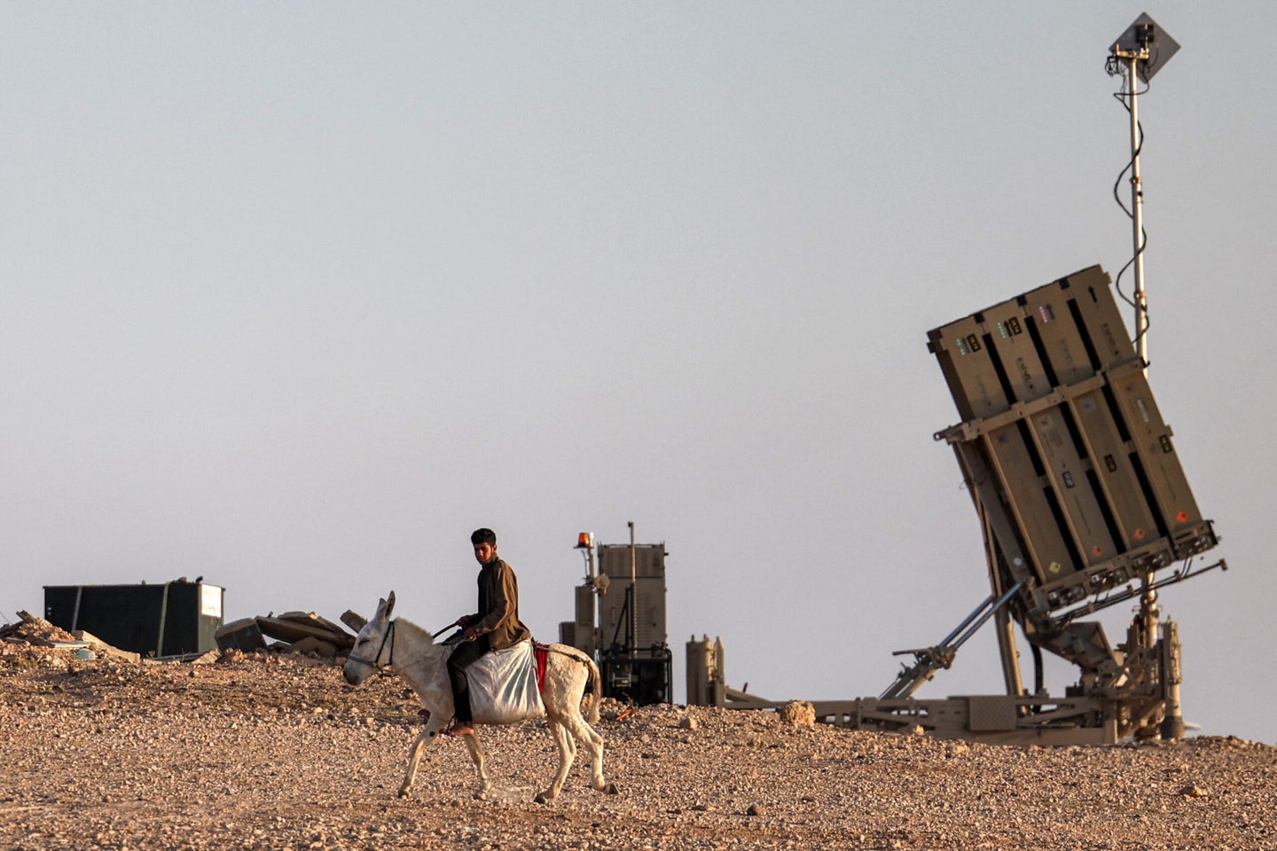 A boy rides a donkey near one of the batteries of Israel's Iron Dome missile defence system at a village not recognised by Israeli authorities in the southern Negev desert on April 14, 2024. (Photo by AHMAD GHARABLI / AFP) (Photo by AHMAD GHARABLI/AFP via Getty Images)
