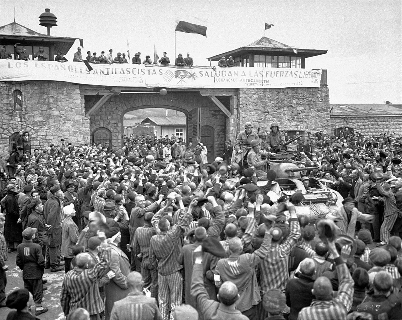 An M8 Greyhound armored car of the US Army's 11th Armored Division entering the Mauthausen concentration camp. The banner in the background (in Spanish) reads as: Anti-fascist Spaniards salute the forces of liberation.