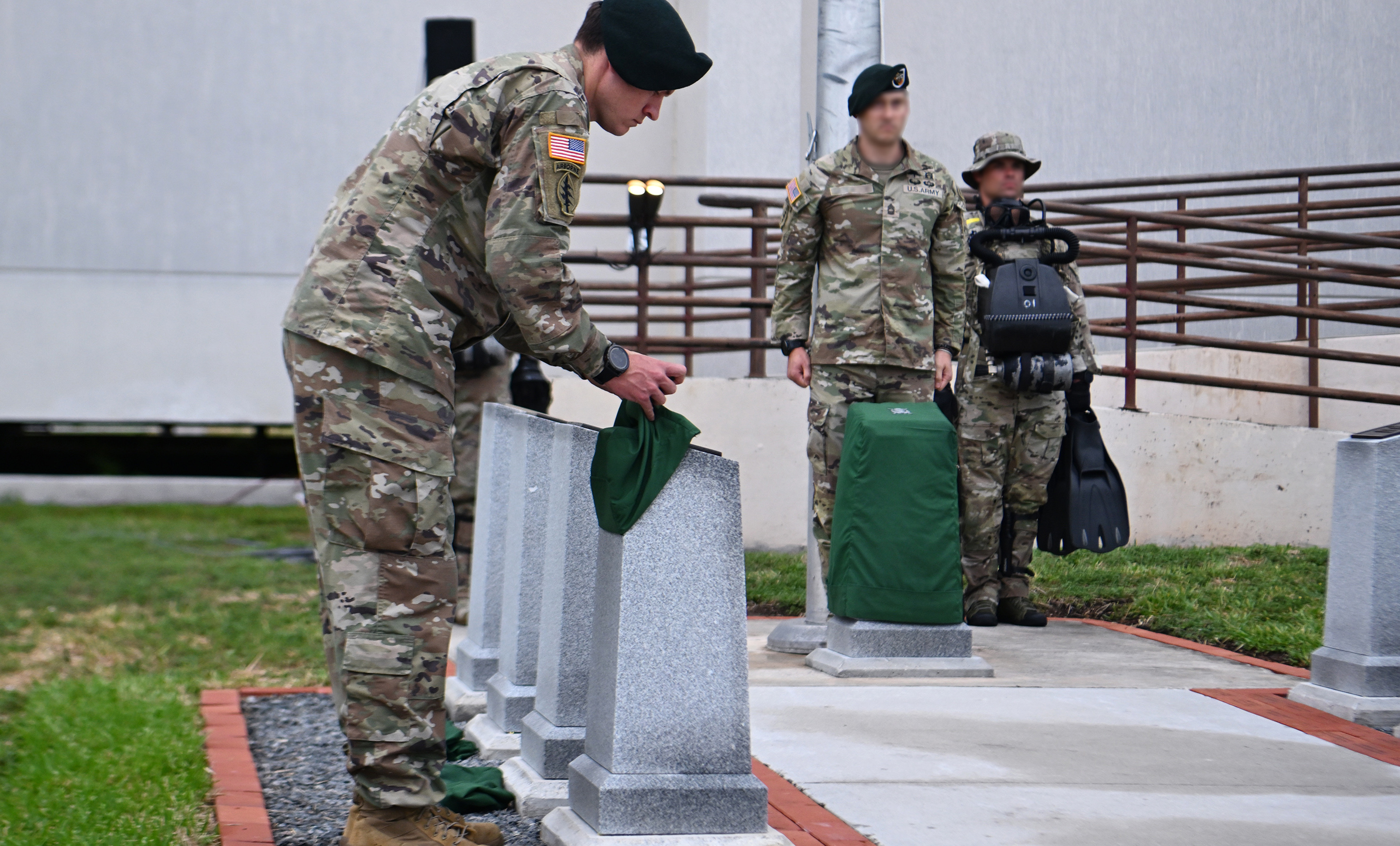 A Soldier from the U.S. Army John F. Kennedy Special Warfare Center and School, removes a cover to reveal a marker honoring a fallen service member during a memorial ceremony at the Special Forces Underwater Operations School at Naval Air Station Key West, Florida, June 11, 2024. The ceremony honored the eight fallen service members who gave their last breath while training at the school which has been operating for more than 60 years. (U.S. Army photo by K. Kassens)