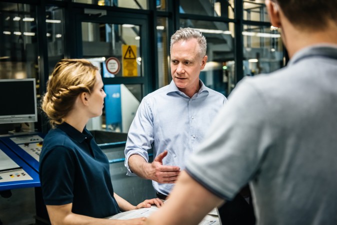 Manager, engineer and trainee talking during a meeting close to a production line in a printery